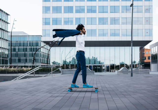 Mann in Business Kleidung aber Turnschuhen auf Skateboard